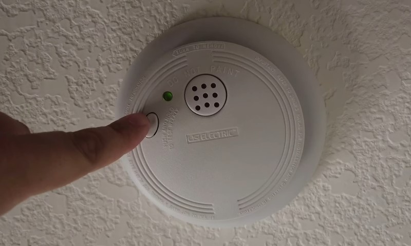 A person pressing the button on a smoke detector to test its functionality